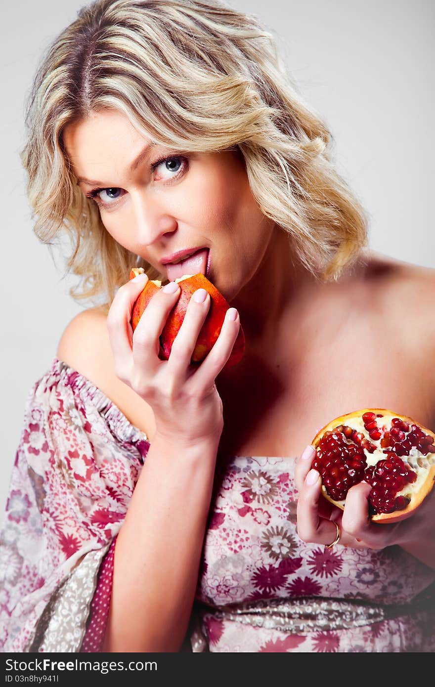 Blonde woman licking pomegranate on grey