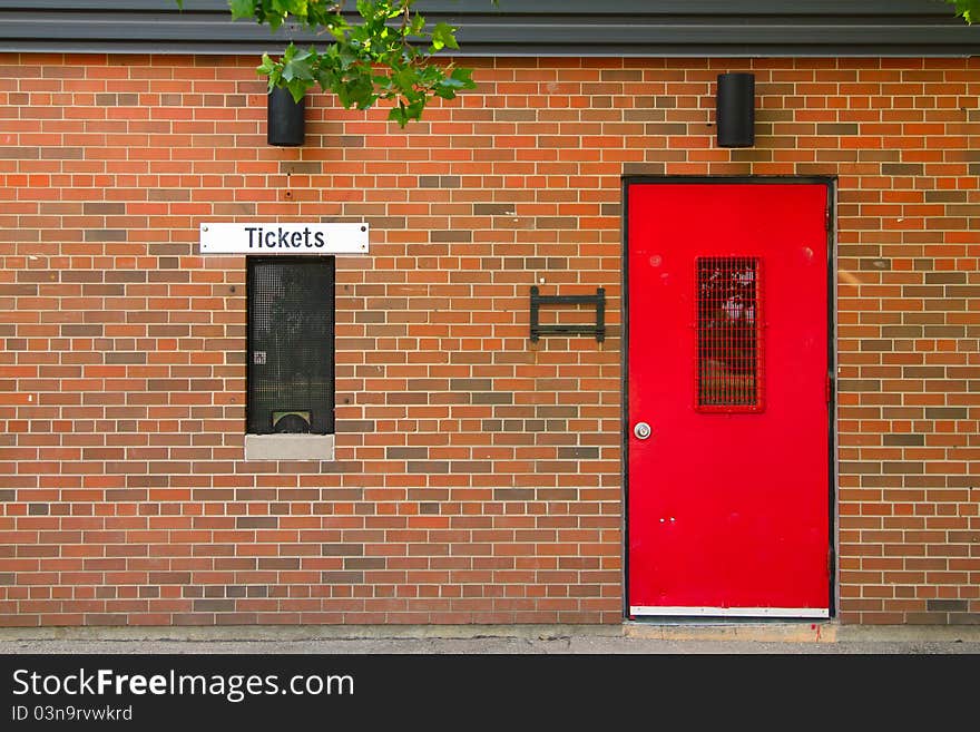 Ticket window and red painted door on the brick background. Ticket window and red painted door on the brick background