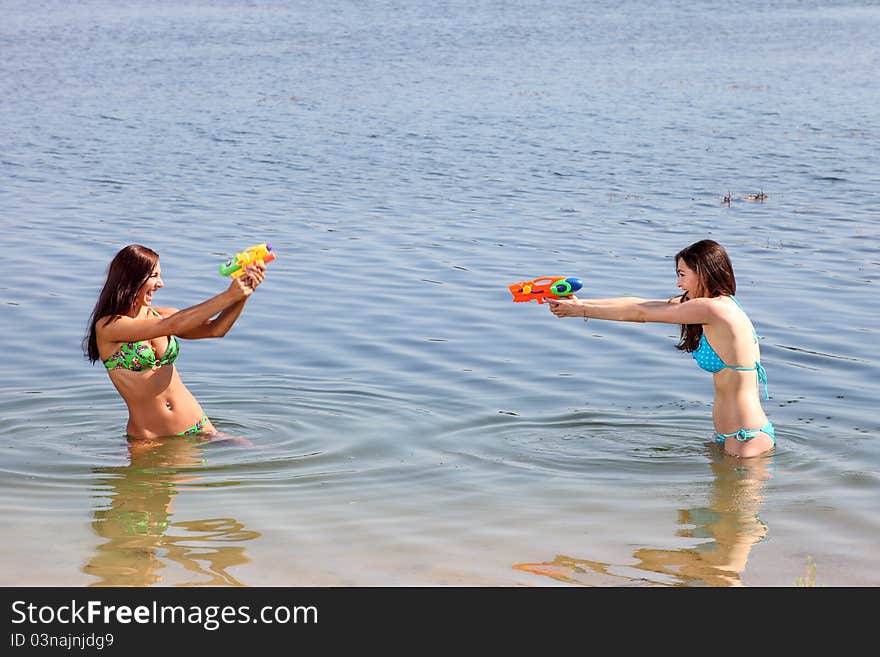 Two girls in bikini play with a water guns