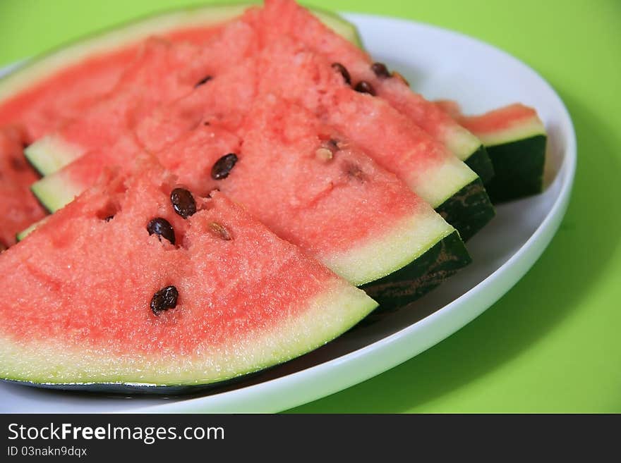 Watermelon white plate on a green background. Watermelon white plate on a green background