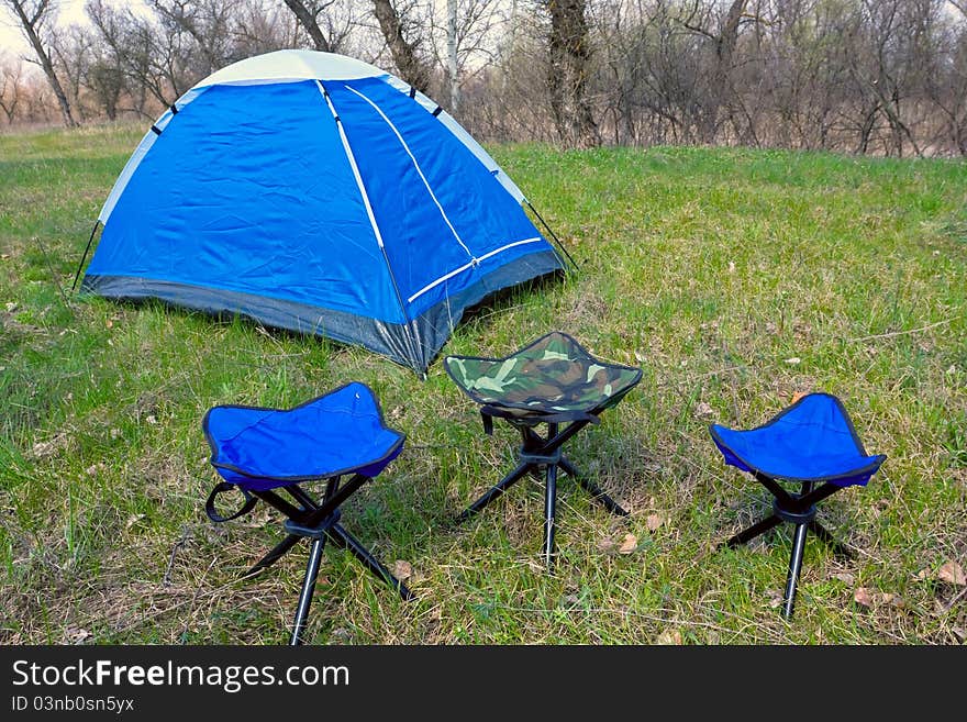 Tourist tent and chairs on green meadow