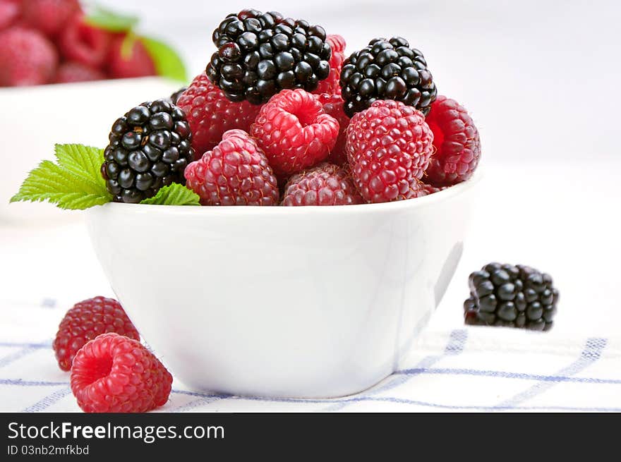 Raspberries and blackberries in a white bowl