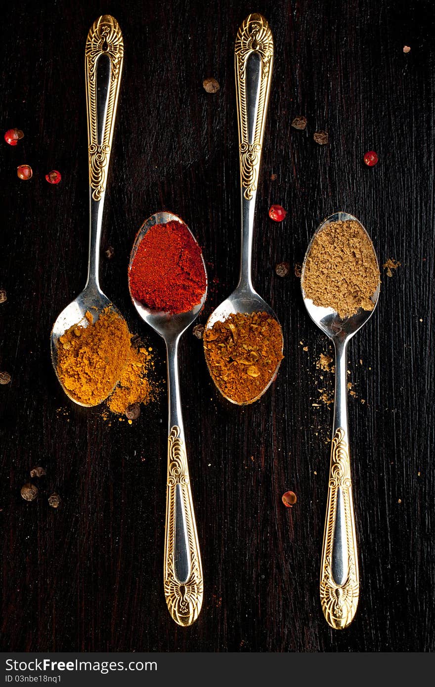 Four silver teaspoons with mix of the spices on black table