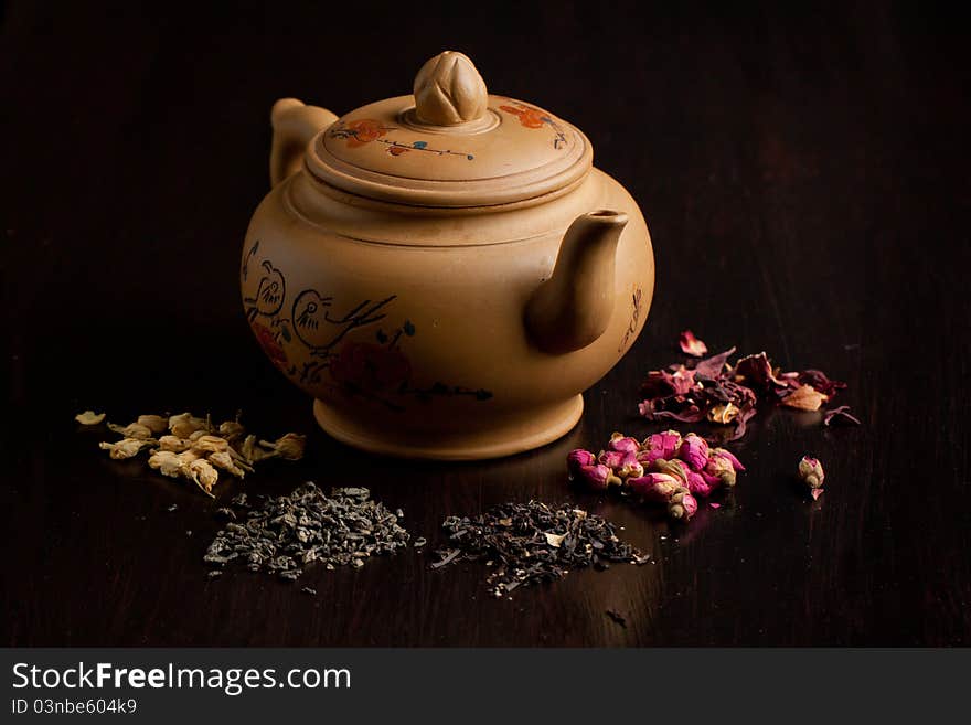 Ceramic teapot with dry tea variation on black table. Ceramic teapot with dry tea variation on black table