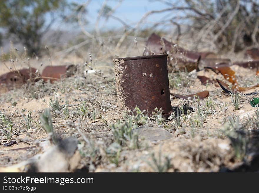 Rusty cans sit in an empty desert field.  A few scattered broken bottles litter the ground as well.