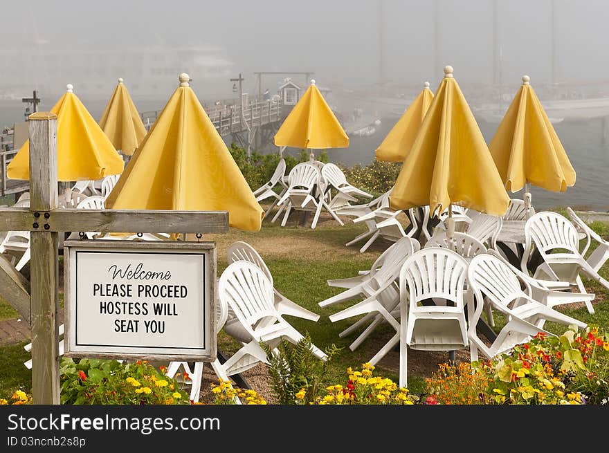 Outdoor cafe or restaurant welcome sign at a New England seaside resort. Ships in foggy background. Outdoor cafe or restaurant welcome sign at a New England seaside resort. Ships in foggy background.