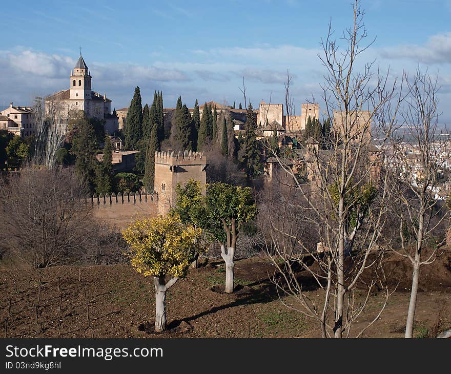 The fortifications of the Alhambra and its surrounding gardens lit up by the early morning sun against a blue sky. The fortifications of the Alhambra and its surrounding gardens lit up by the early morning sun against a blue sky.