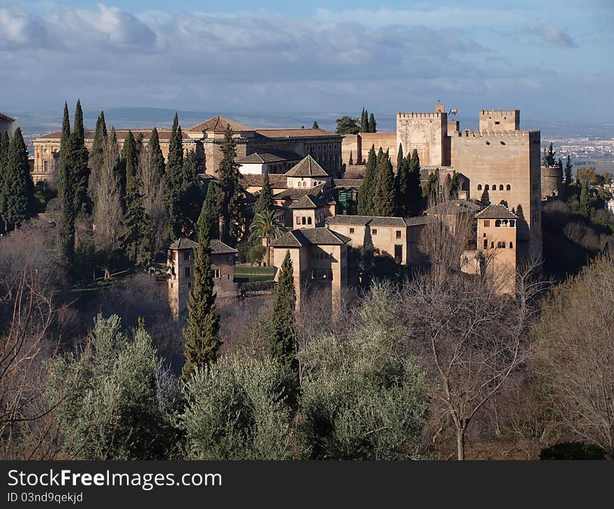 The fortifications of the Alhambra and its surrounding gardens lit up by the early morning sun against a blue sky. The fortifications of the Alhambra and its surrounding gardens lit up by the early morning sun against a blue sky.