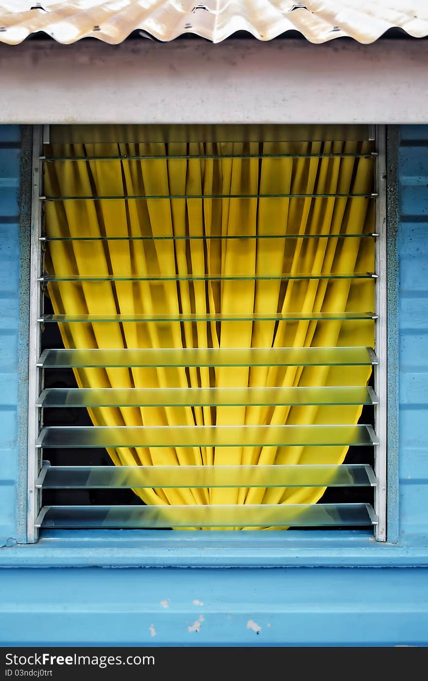 Yellow curtain behind a glass window and a blue wall