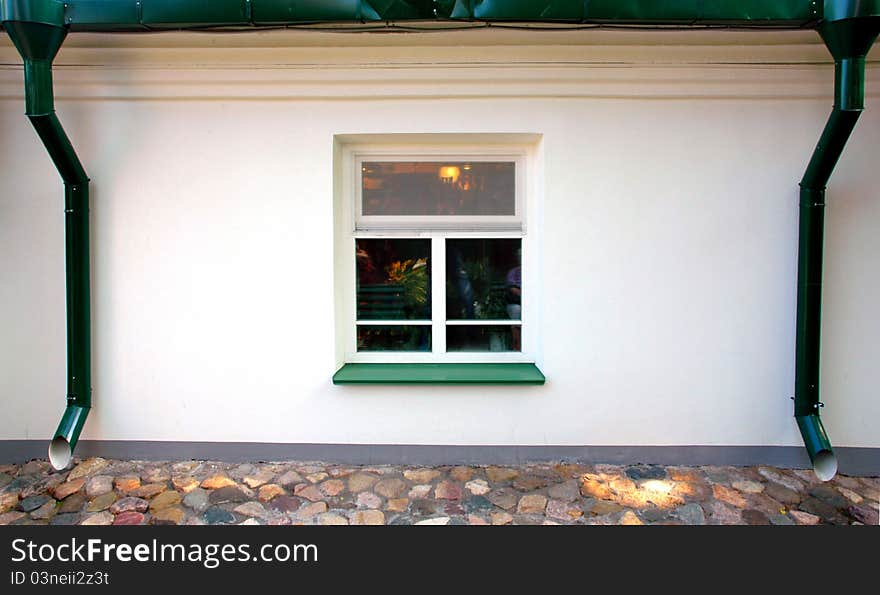 One square window on the white wall, two green downspouts. One square window on the white wall, two green downspouts.