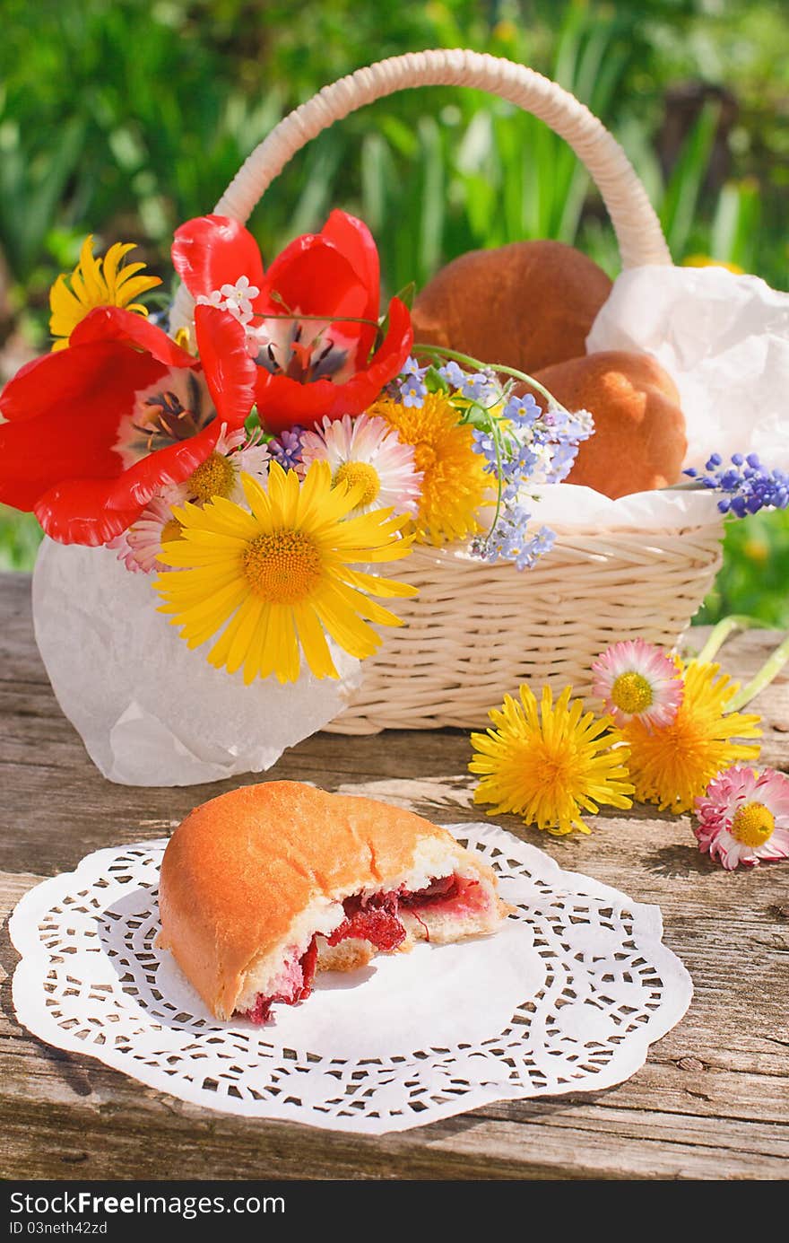 Bitten off a cherry pie and basket with flowers on the old table in the garden in summer day. Bitten off a cherry pie and basket with flowers on the old table in the garden in summer day