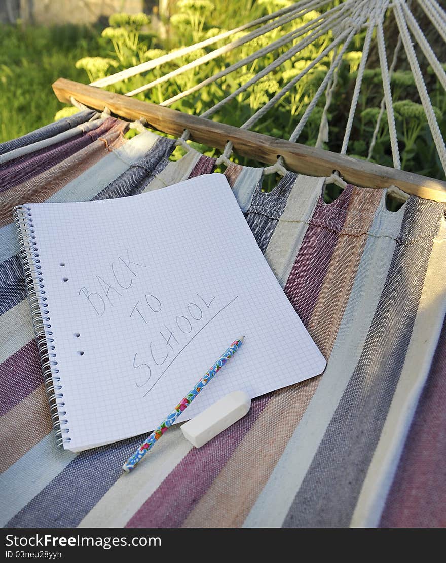 Paper and pencil with written phrase back to school in a hammock symbolizing end of summer holiday or start of semester.