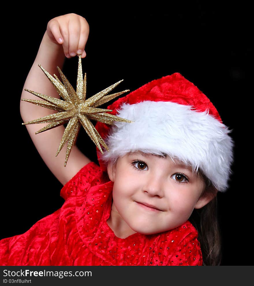 Adorable girl in Christmas outfit playing with golden star ornament. isolated on black. Adorable girl in Christmas outfit playing with golden star ornament. isolated on black