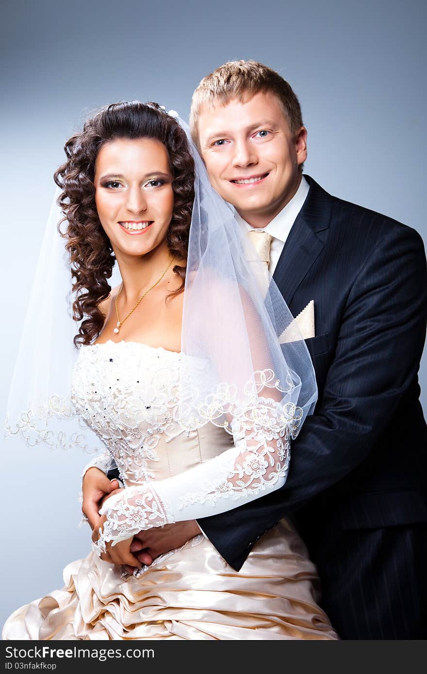 Studio portrait of young elegant enamoured just married bride and groom and embracing on grey background. Studio portrait of young elegant enamoured just married bride and groom and embracing on grey background