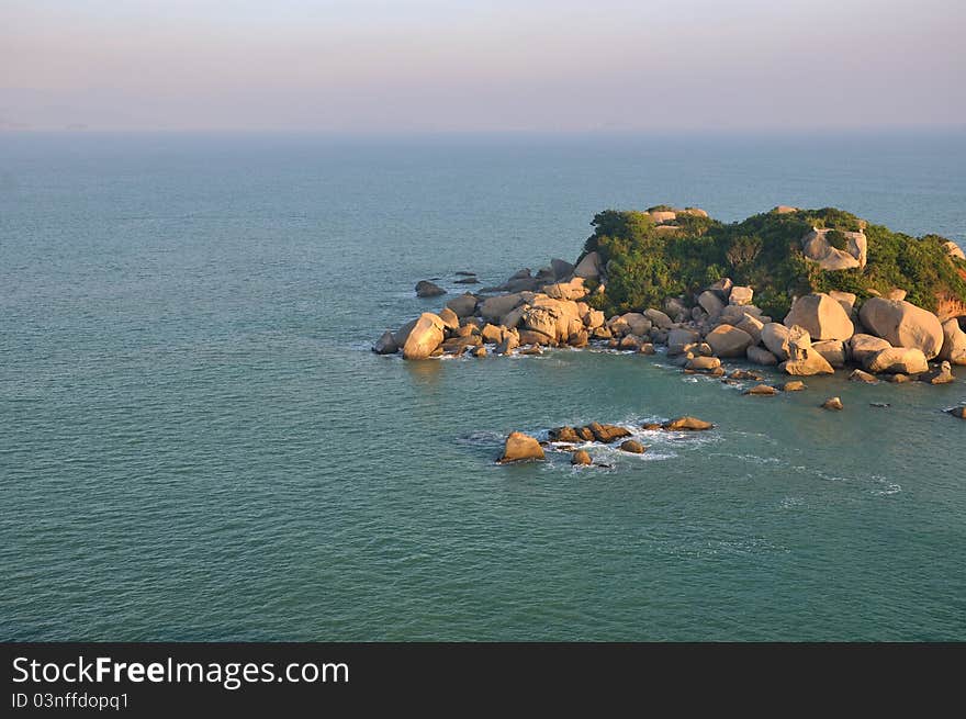 Small rock island under warm sunrise lighting among blue sea water, shown as color and texture comparing between sky, water and rock. Small rock island under warm sunrise lighting among blue sea water, shown as color and texture comparing between sky, water and rock.