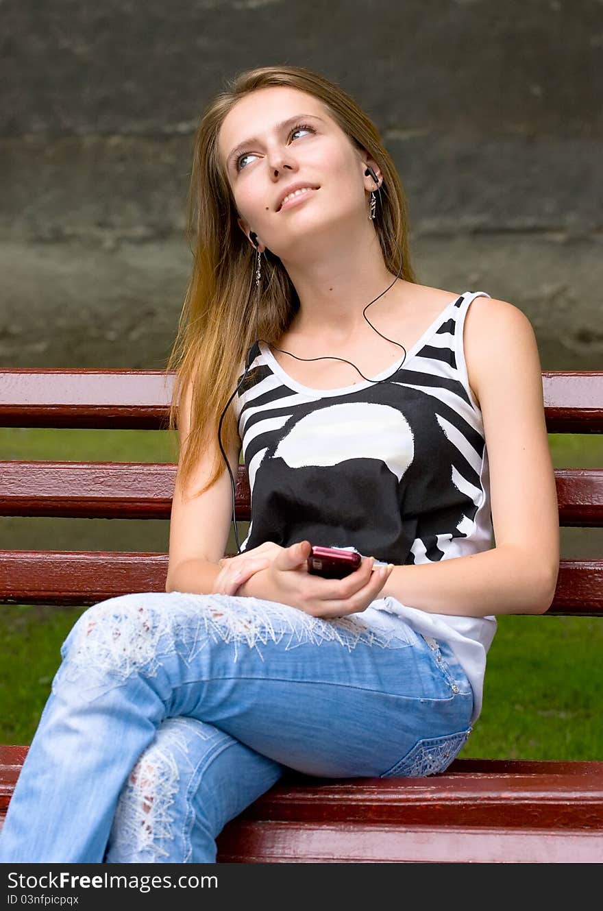 Cute attractive girl is listening music in earphones plugs on mp3 player or mobile phone. Cute attractive girl is listening music in earphones plugs on mp3 player or mobile phone