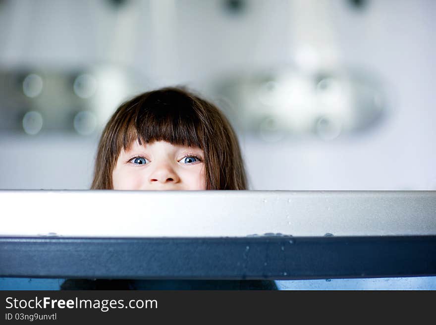 Child girl plays in a bathtub while looking out over a side