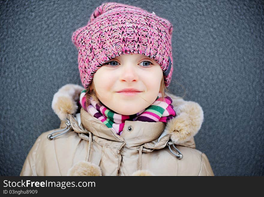 Smiling child girl wearing pink knitted hat and striped scarf. Smiling child girl wearing pink knitted hat and striped scarf