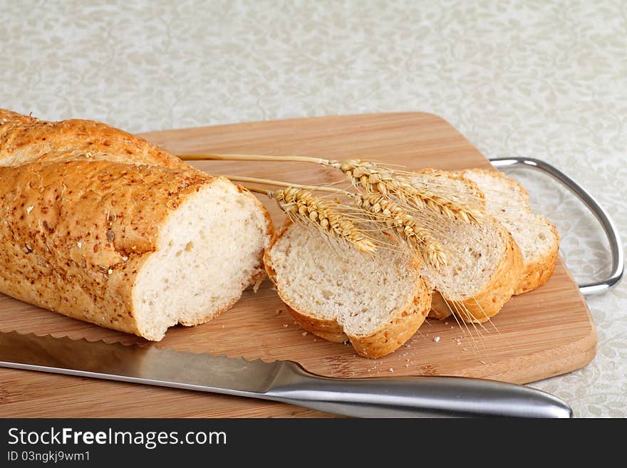 Sliced wheat bread with wheat heads on a cutting board. Sliced wheat bread with wheat heads on a cutting board