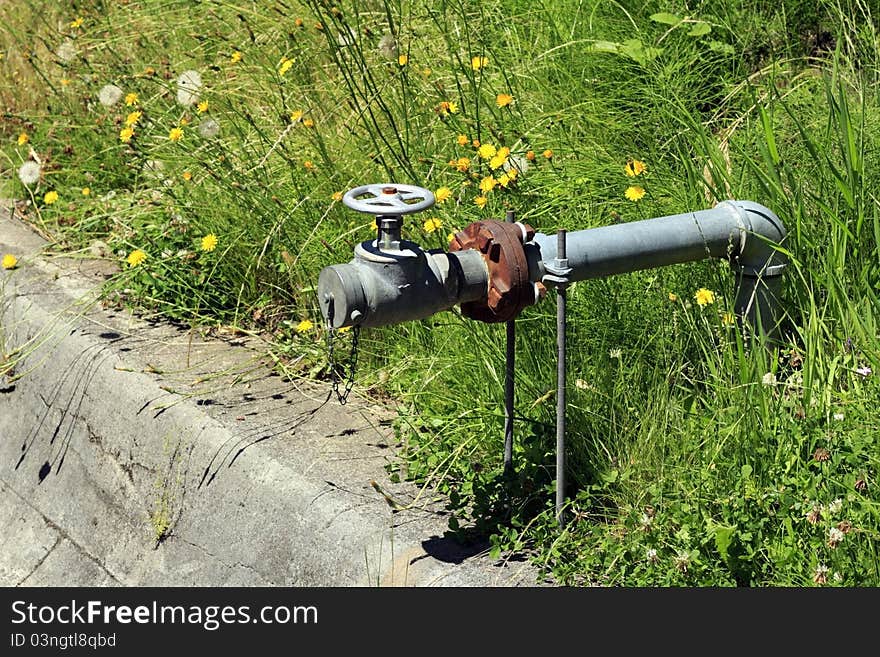 Old water pipe with valve wheel in some weedy grass. Old water pipe with valve wheel in some weedy grass.