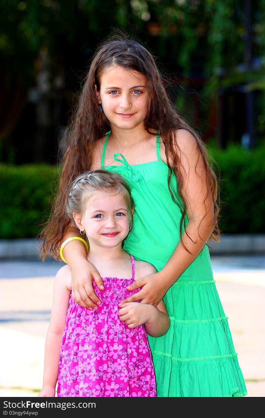 Two little girls,(sisters) holding each-other outdoor looking at the camera. Two little girls,(sisters) holding each-other outdoor looking at the camera