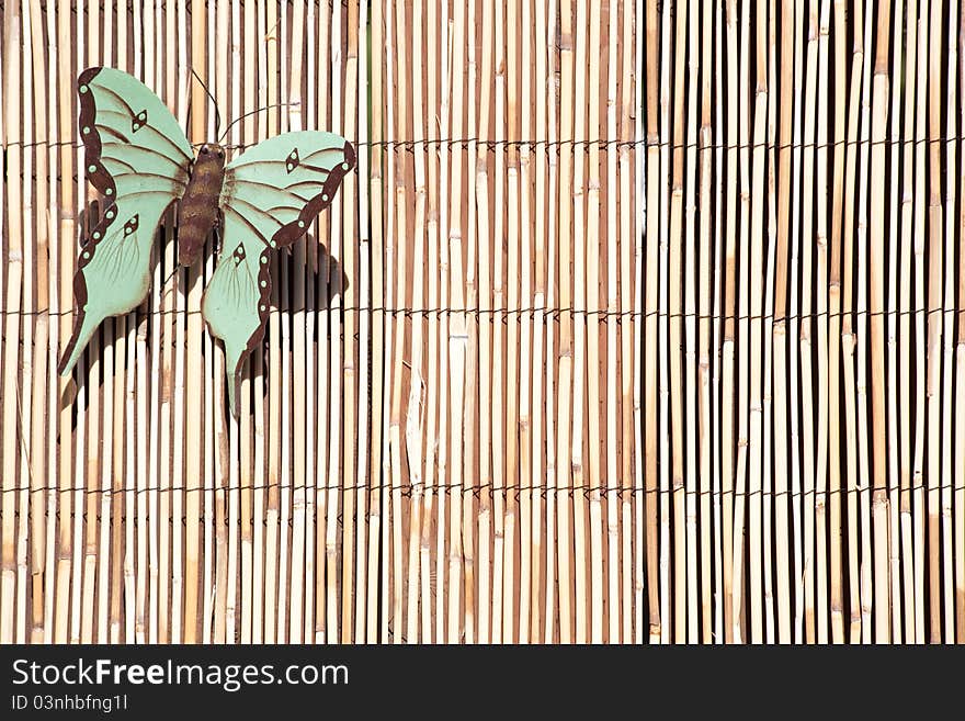 An artistic metal butterfly sits on a bamboo fence in an urban yard.