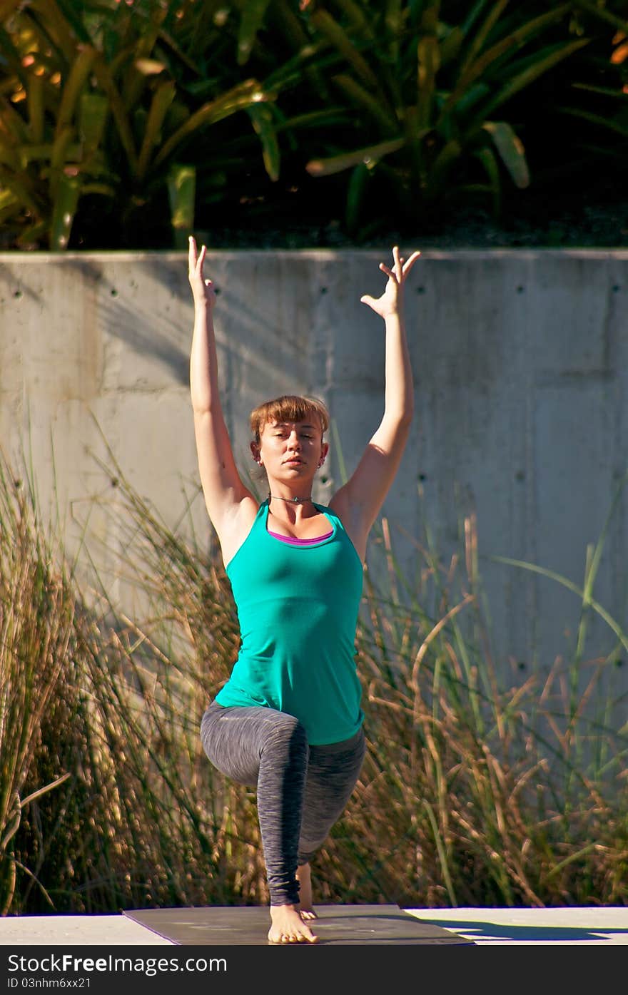 An athletic brown haired woman is doing yoga exercise Virabhadrasana or warrior 1 pose outside in park in direct sunlight. An athletic brown haired woman is doing yoga exercise Virabhadrasana or warrior 1 pose outside in park in direct sunlight.