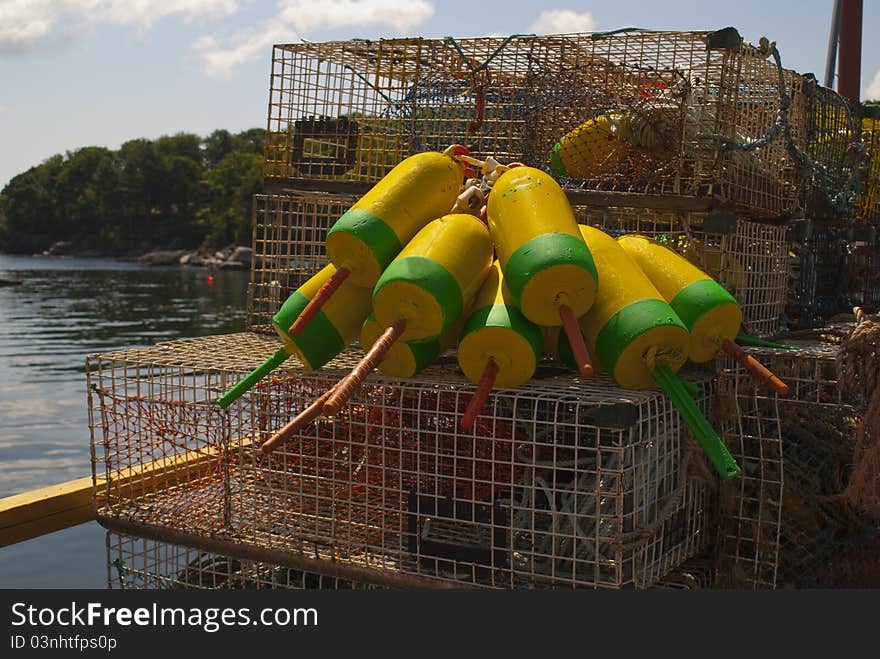 Yellow and green lobster floats are tied to a large stack of lobster traps sitting on the pier with ocean harbor in the background. Yellow and green lobster floats are tied to a large stack of lobster traps sitting on the pier with ocean harbor in the background.