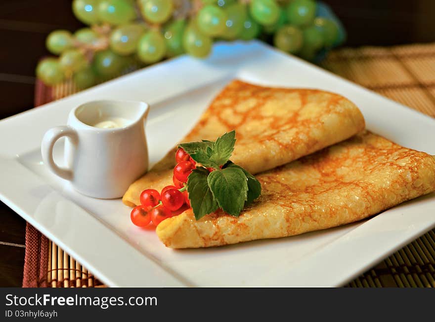 Russian pancakes with sour cream, redcurrant and mint