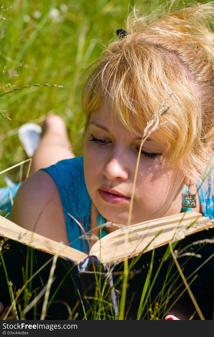 Blonde girl in grass with book