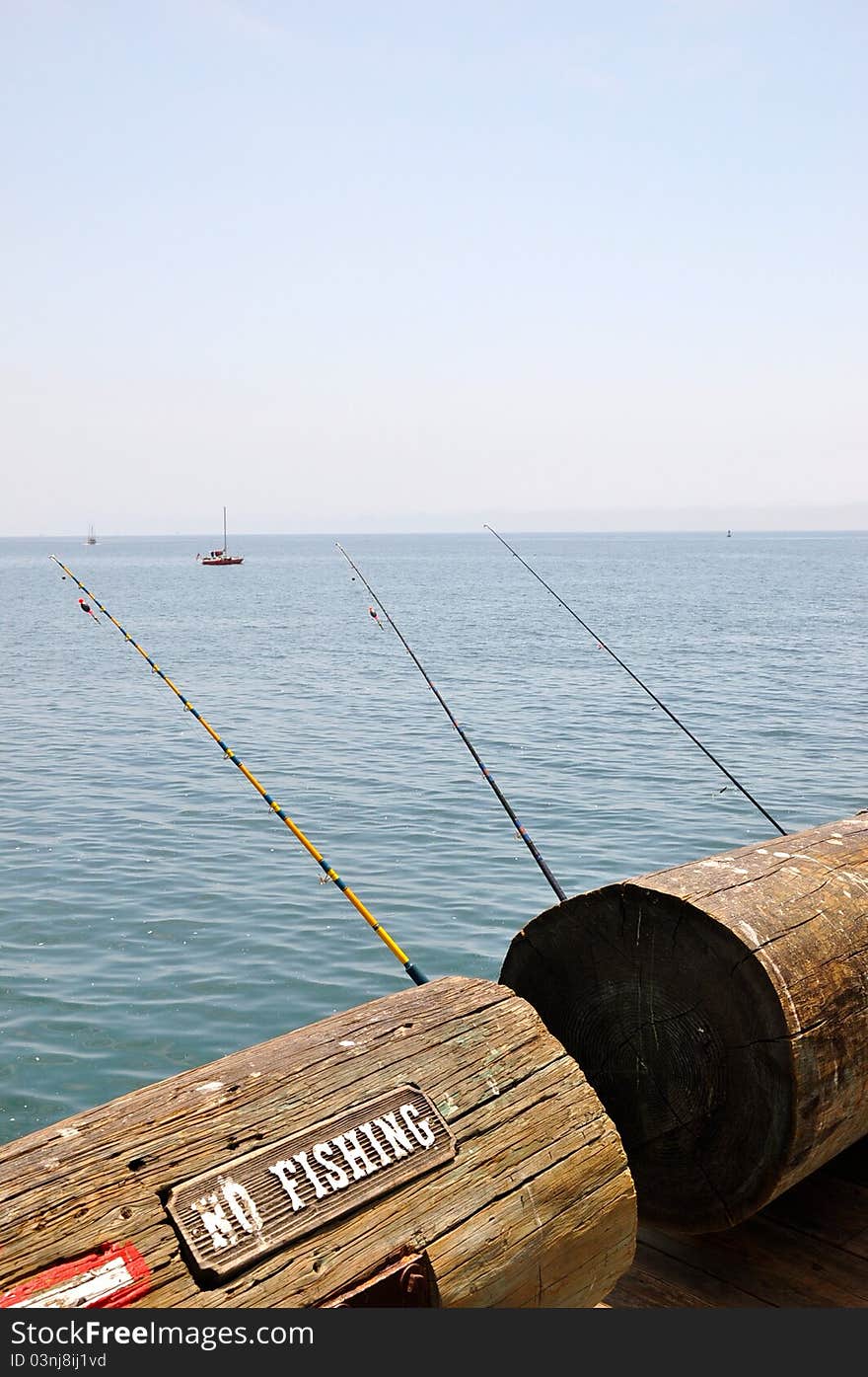 A view of fishing poles on Santa Barbara Pier, California. Contrasting image against a no fishing sign.