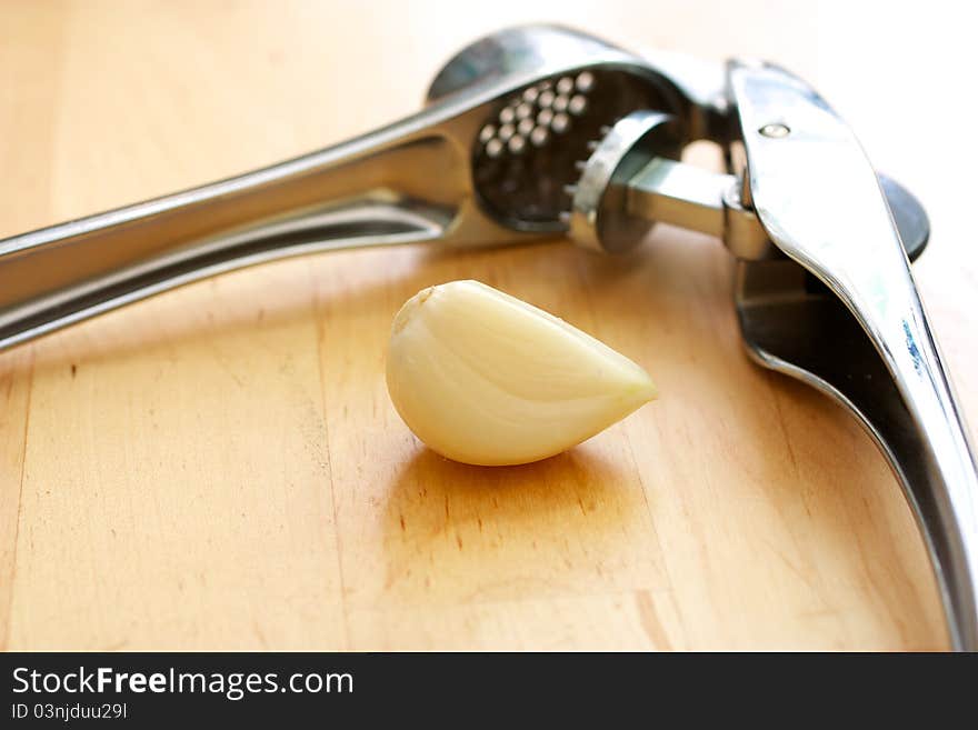 Garlic masher lies on a wooden table next to the garlic clove.