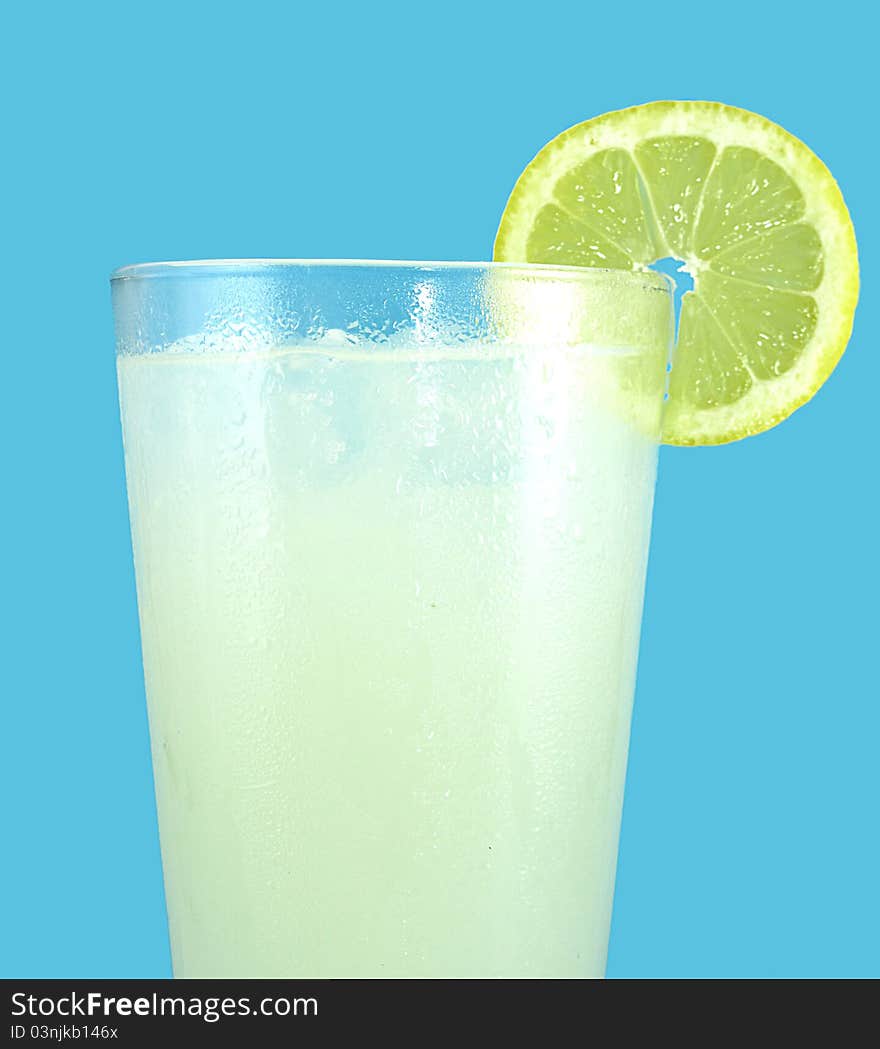 Ice cold glass of freshly squeezed lemonade with a slice of lemon isolated on an aqua cyan background.