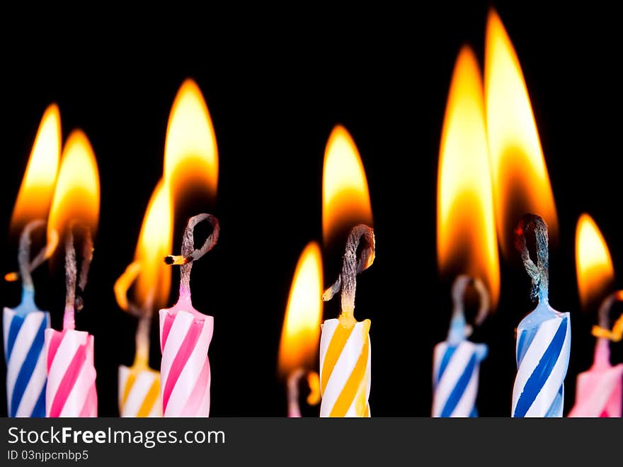 Many coloured candles burn before black background