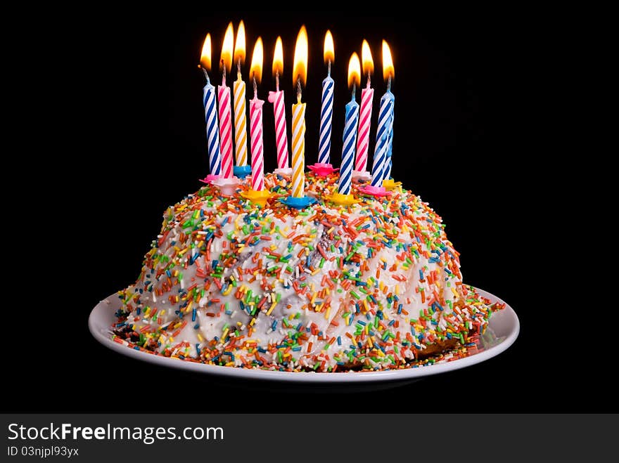 A cake with many coloured candles before black background. A cake with many coloured candles before black background