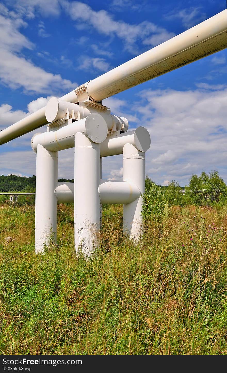 The high pressure pipeline in a summer landscape with the dark blue sky and clouds