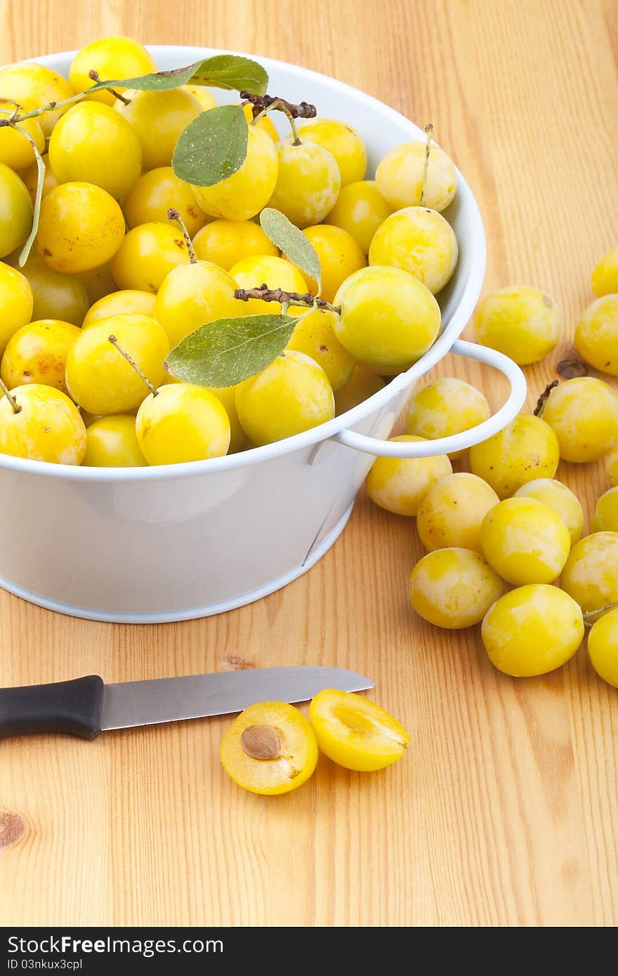 Studio-shot of small yellow plums also known as mellow mirabelles, on a wooden countertop. one is halved with a knife.