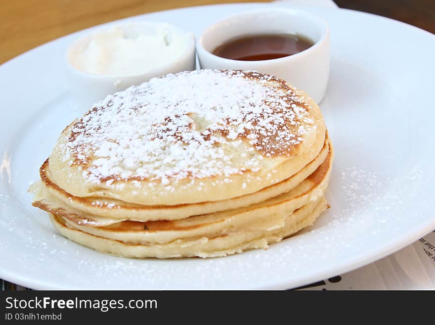 Pancakes on a white plate with sour cream and maple syrup