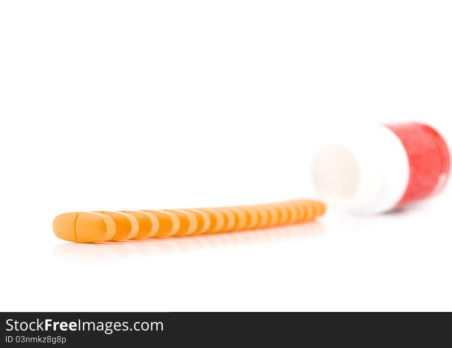 Vitamins are poured out in a row from a small bottle on a white background