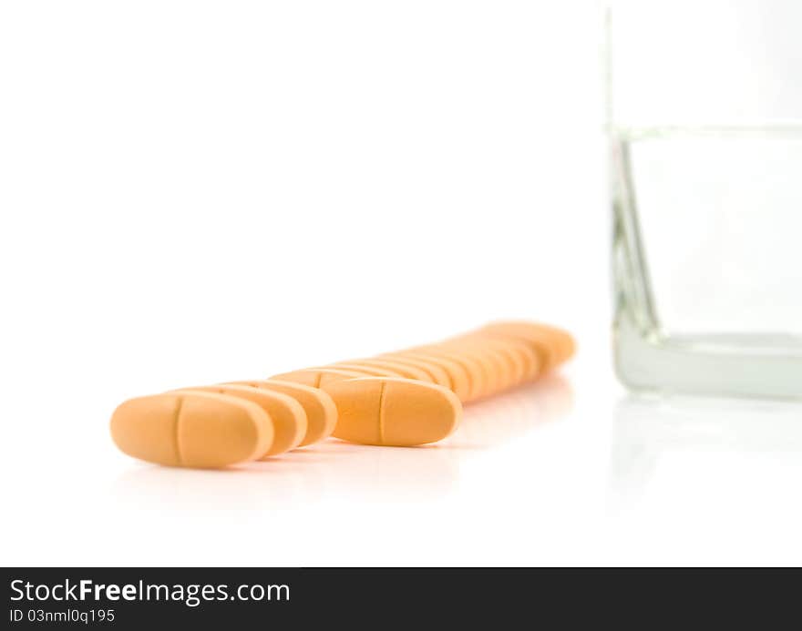 Vitamins lie in a row with glass of water on a white background