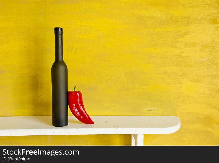 Black bottle and red pepper on yellow background