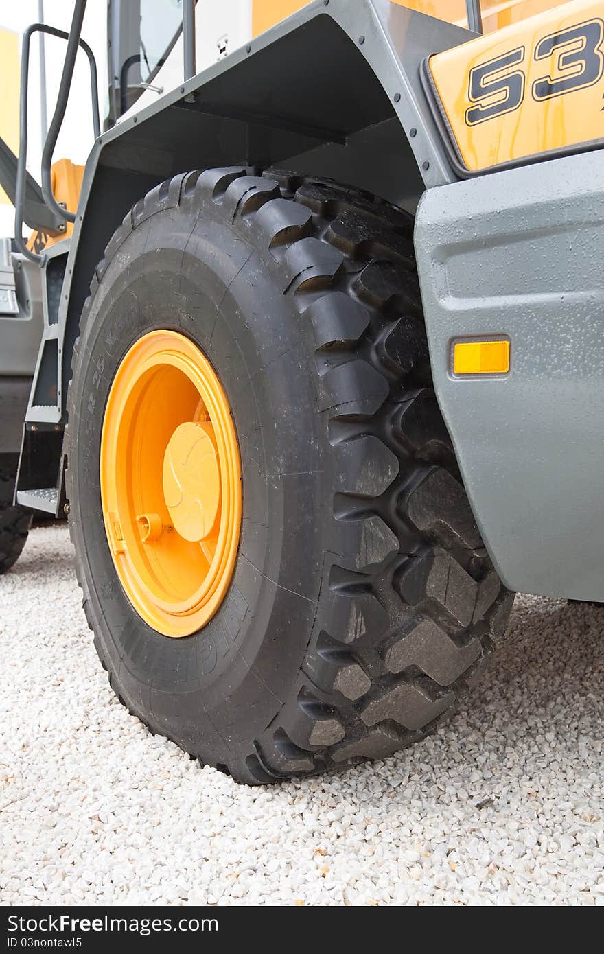 Black wheel with yellow disk of front loader on white stone road