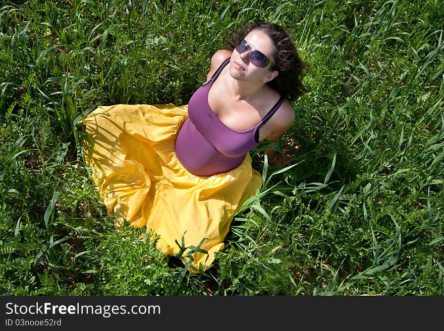 Pregnant woman on green grass field under blue sky in summer