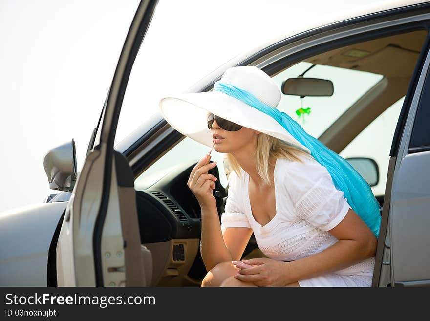 Woman putting lipstick on using the car mirror