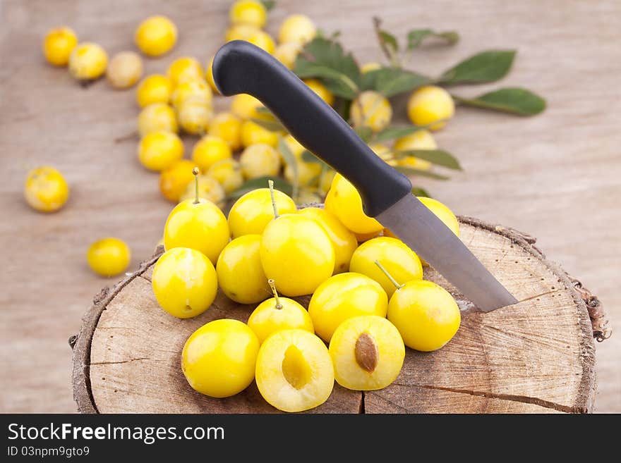 Studio-shot of small yellow plums also known as mellow mirabelles, on a tree trunk. one is halved with a knife.