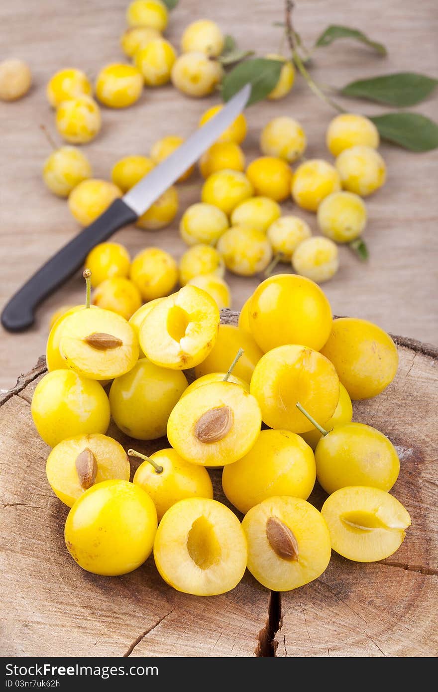 Studio-shot of small yellow plums also known as mellow mirabelles, on a tree trunk. some are halved with a knife.