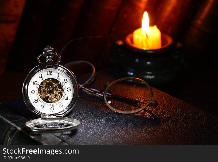 Vintage pocket watch near spectacles and candle on dark background. Vintage pocket watch near spectacles and candle on dark background