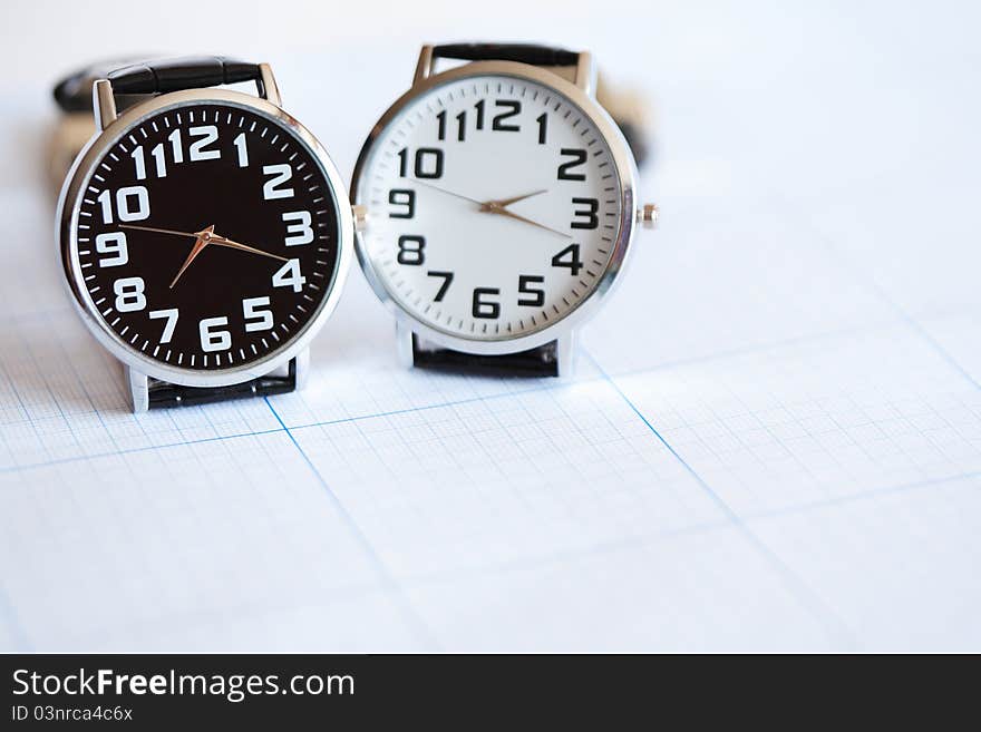 Pair of modern wristwatches standing on graph paper surface. Pair of modern wristwatches standing on graph paper surface