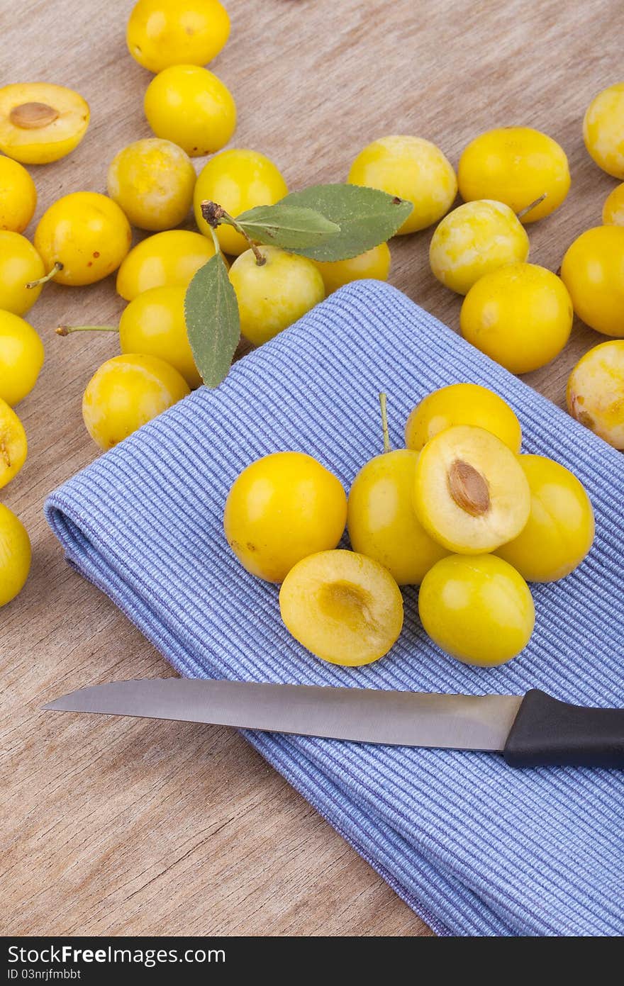 Studio-shot of small yellow plums also known as mellow mirabelles, on a table napkin. one is halved with a knife.