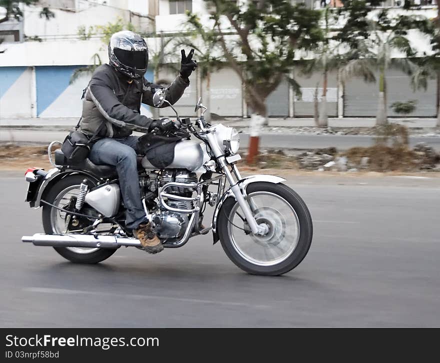 Motor biker breaks road rules by undertaking on the inside lane, horizontal landscape, copy space and crop space. Tarmac roads with white markings, derelict factory on roadside undergrowth. Motor biker breaks road rules by undertaking on the inside lane, horizontal landscape, copy space and crop space. Tarmac roads with white markings, derelict factory on roadside undergrowth